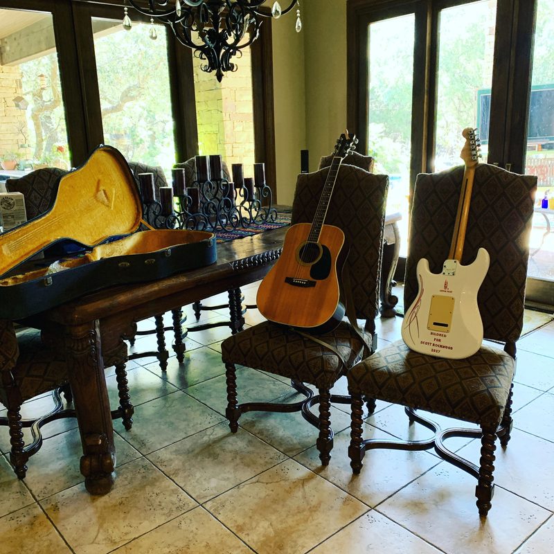 An acoustic guitar and a white electric guitar waiting on dining chairs before a show