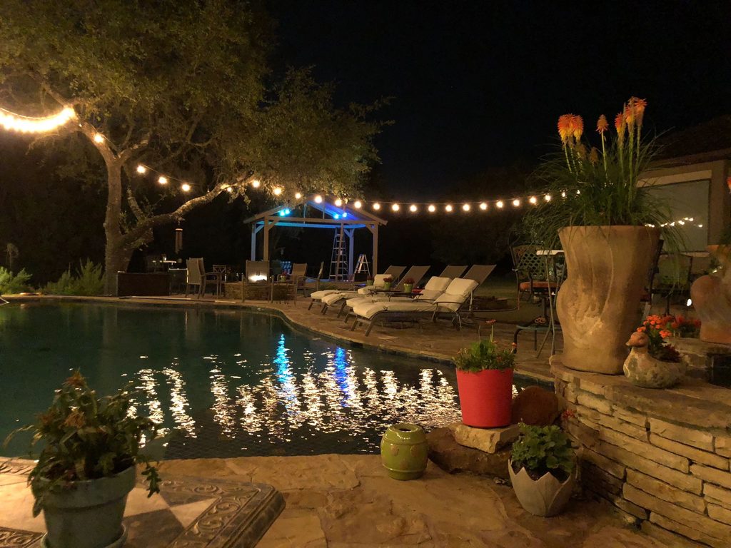 The backyard at night: string lights over the pool and the gazebo stage under the oaks